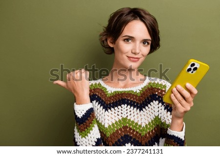Photo portrait of lovely young lady gadget point empty space dressed stylish print knitted clothes isolated on khaki color background