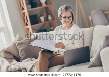 Photo of confident good mood elderly lady boss wear white cardigan reading papers modern device indoors apartment room