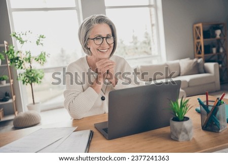Photo of smiling shiny elderly lady advisor wear white cardigan chatting modern device indoors apartment room