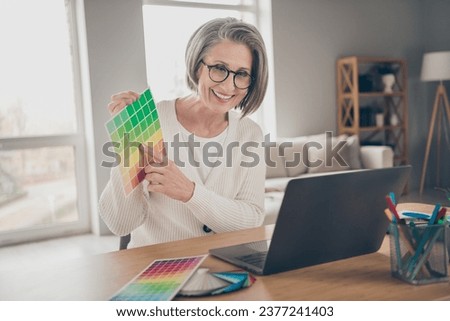 Photo of sweet shiny elderly lady designer wear white cardigan showing modern device colors palette indoors apartment room