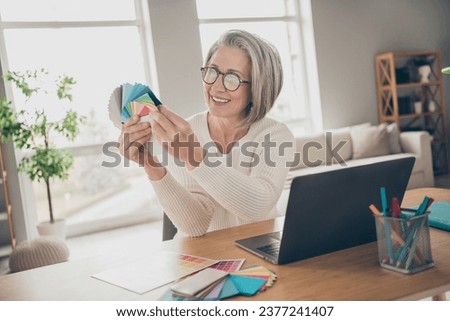 Photo of adorable pretty elderly lady wear white choosing design colors samples indoors apartment room