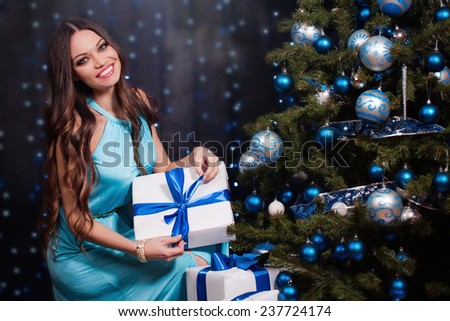 Beautiful young woman with present near christmas tree