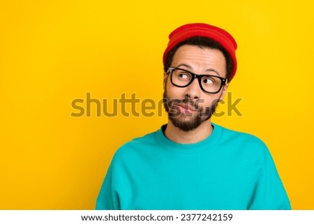 Photo of minded puzzled cool man wear teal sweatshirt red beanie hat thoughtfully look empty space isolated on yellow color background