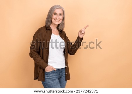 Photo of satisfied nice woman dressed brown shirt directing at offer empty space arm in pocket isolated on pastel color background