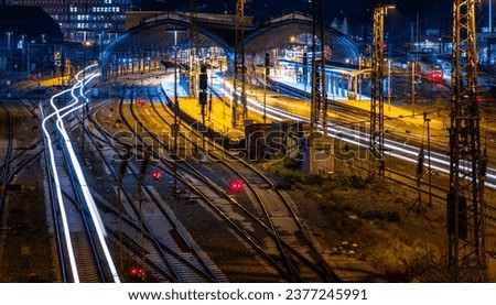 Main station with many tracks, platforms, hall, signals and light traces of passing passenger trains in Hagen, Germany. Colorful early morning twilight atmosphere with longtime exposure from bridge. Royalty-Free Stock Photo #2377245991