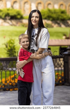 Mom and son are on vacation in the park, the woman hugs her son tightly.