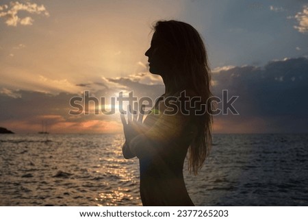 Side view of silhouette of anonymous woman meditating with clasped hands near rippling sea during sunset while standing in tadasana and doing yoga Royalty-Free Stock Photo #2377265203