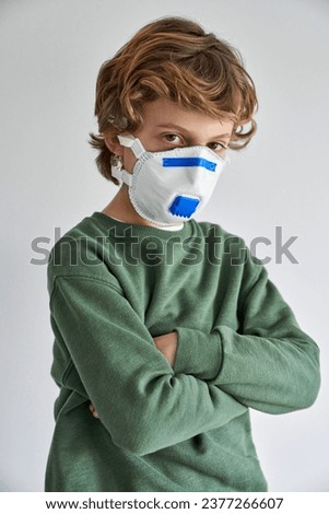 Preteen child in green sweater and medical respirator with arms crossed self isolating maintaining quarantine and looking at camera
