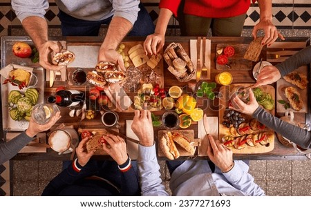 Top view group of anonymous friends eating appetizing various snacks on cutting boards while sitting at wooden table in kitchen Royalty-Free Stock Photo #2377271693