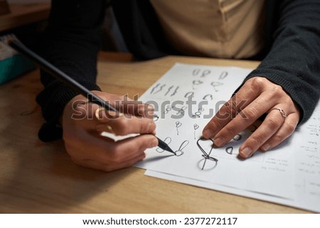 High angle of crop unrecognizable jeweler creating pictures of rings with pencil on paper sheet on wooden table