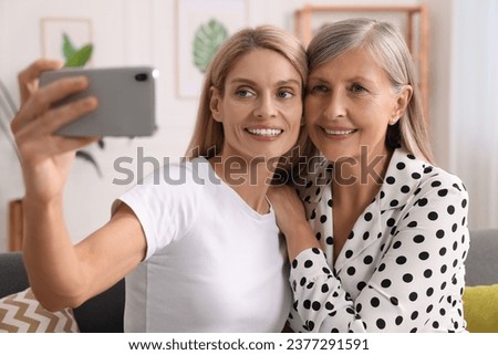 Happy daughter taking selfie with her mature mother at home