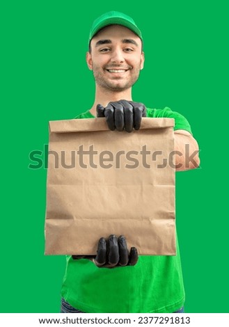 Delivery man with paper bag. Courier in uniform cap and t-shirt, gloves service fast delivering orders. Young guy holding a cardboard package. Character on isolated background for mockup design. Royalty-Free Stock Photo #2377291813