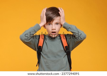 Surprised schoolboy covering head with hands on orange background Royalty-Free Stock Photo #2377294091
