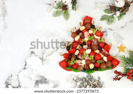 Christmas and New Year's dishes, a set of snacks for the festive table. Plate with Christmas tree of tomatoes, pate, mozzarella cheese, salami, olives, black olives and grapes on a concrete table, 