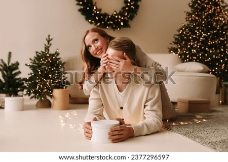 A man and a woman in love give each other Christmas gifts and congratulate on holidays in the decorated interior of a cozy room in the new year at home in winter. Selective focus