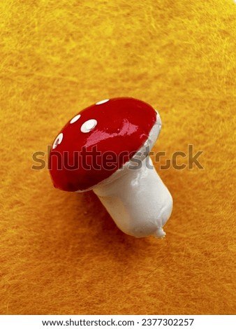 A small plastic button in the shape of a fly agaric mushroom with a white stem and a red cap with white spots. Lies on a white background. Used to decorate children's clothing. One joke. Close-up.