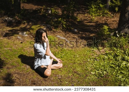 Om chanting, mind calming practice, girl doing yoga, hatha yoga in nature, lotus pose sitting on the grass, unity with nature. Royalty-Free Stock Photo #2377308431