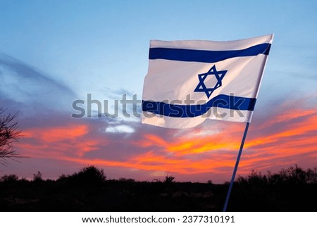 
Israel flag against the backdrop of a fiery sunset. Remembrance Day - Yom HaZikaron, Patriotic holiday, Israeli Independence Day - Yom Ha'atzmaut concept. Royalty-Free Stock Photo #2377310191