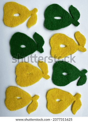 Green and yellow decorative pears with a tail and a leaf on top, made of felt with a hole in the center. They are used to decorate a children's room. Close up.
