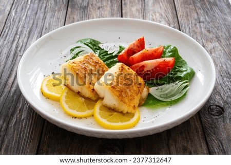 Seared cod loin and fresh vegetables on wooden table 
