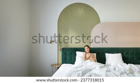 Vertical shot of beautiful asian girl lying in bedroom with sophisticated interrior, smiling and looking happy in morning, spending time in bed. Royalty-Free Stock Photo #2377318015