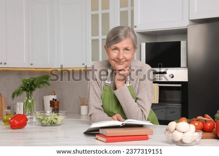 Happy woman with recipe book at table in kitchen