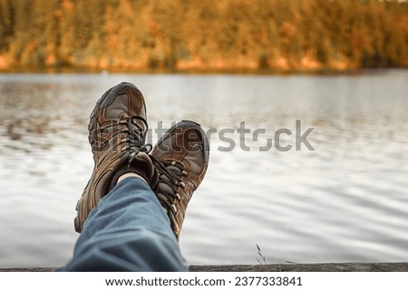 Man with hiking shoes relaxing by an autumn mountain lake. Adventure and people finding peace alone in nature 