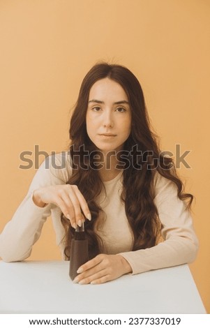 Pretty woman holding bottle of cosmetics isolated on beige background.