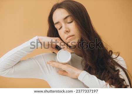 Fashion portrait of a beautiful woman with a bottle of cosmetic cream on a beige pastel background.