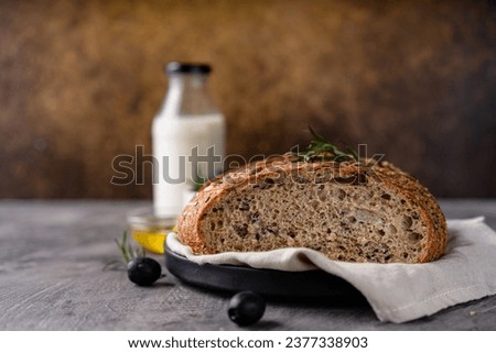 Freshly baked sourdough bread from whole grain flour and pumpkin seeds on a grid, olive oil and black olive on a rustic wooden table. Artisan bread.