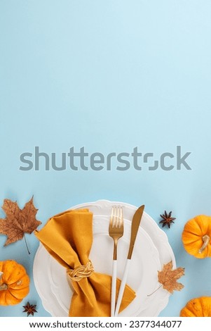 Prepare a Thanksgiving table that's worth recalling. Top view vertical shot of plates, cutlery, ripe pumpkins, anise, autumn leaves on soft blue background with commercial placeholder