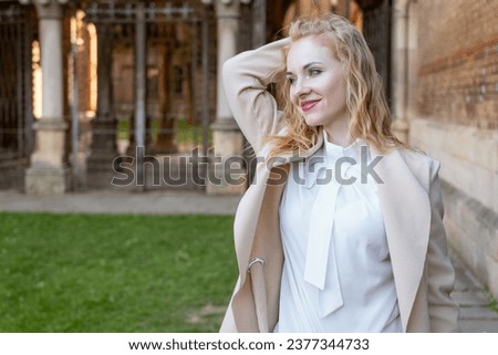 Portrait of attractive red-haired girl in spring outdoors. Cute blonde girl in white blouse and coat outside smiling and looking at the camera.