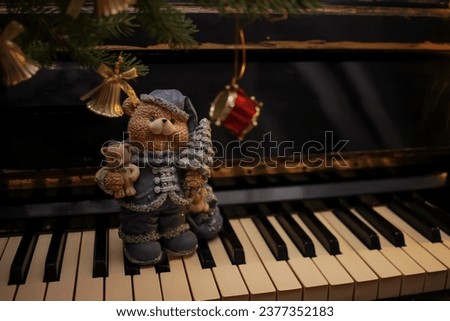 Decorative figurine of a fairy bear with a Christmas tree on a piano, decorated with a fir tree and bells. Festive new year decor, warm dark composition