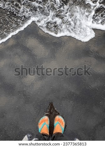This is a picture of a beachgoer's feet standing at the water's edge, waiting for the waves to come.
