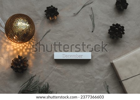 Word December on calendar by background with spruce branches and a glowing garland. Christmas, winter, new year concept