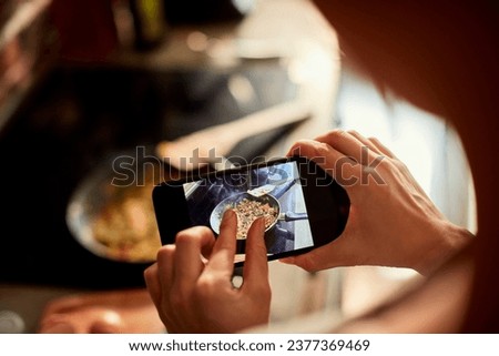 Close up of a woman holding smartphone taking picture of a meal being cooked in the kitchen
