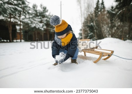 Funny toddler boy having fun with a sleigh in beautiful winter park. Cute child playing in a snow. Winter activities for kids.
