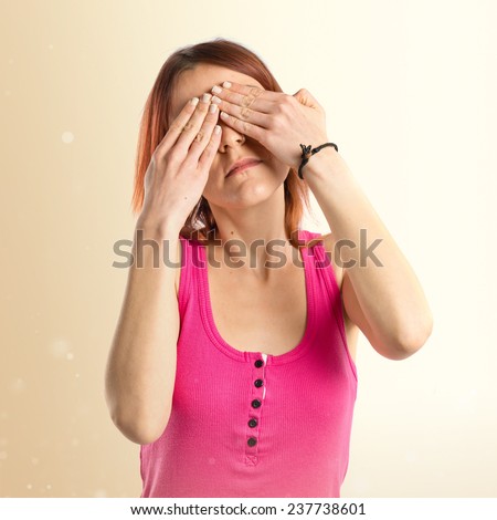 young girl covering her eyes over ocher background 