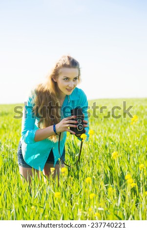 young blond woman with vintage medium format photo camera in a green wheat field taking a photo