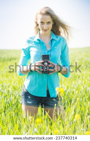 young blond woman with vintage camera on a summer green wheat field who feels inspiration and takes pictures