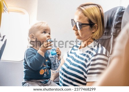 Mom and child flying by plane. Mother holding and playing with her infant baby boy child in her lap during economy comercial flight. Concept photo of air travel with baby. Real people Royalty-Free Stock Photo #2377468299