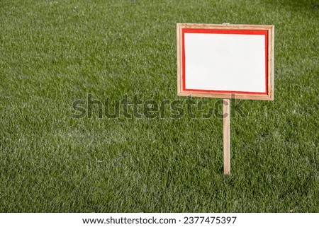 Pointer sign on a lawn with green grass. Banner mockup with place for text. Information board on the green lawn.
Empty board on green lawn