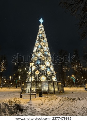 A Christmas tree decorated with neon garlands stands on the square in winter in the city.