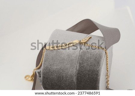 A gold bracelet featuring a pendant engraved with the words draped over a textured grey fabric, accompanied by a subtle gold charm, against a soft white background.