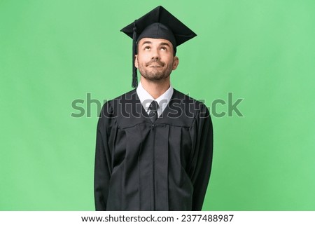 Young university graduate man over isolated background and looking up