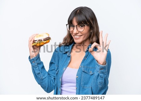 Young caucasian woman holding a burger isolated on white background showing ok sign with fingers