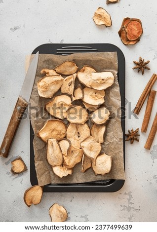 Dried pear slices on baking tray with cinnamon on light table. Royalty-Free Stock Photo #2377499639