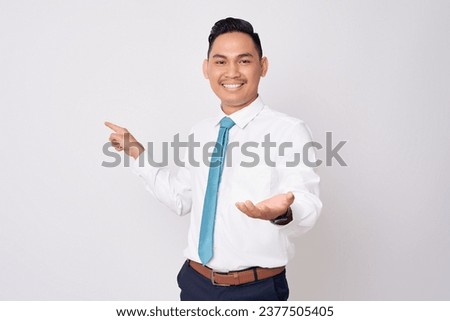 Smiling happy young Asian businessman wearing a formal shirt and tie pointing a finger at blank screen and showing palm up gesture isolated on white background