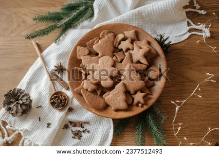 Christmas gingerbread cookies in wooden plate on rustic table flat lay with fir branches, pinecone, spices. Merry Christmas! Delicious fresh gingerbread cookies close up, atmospheric holiday Royalty-Free Stock Photo #2377512493