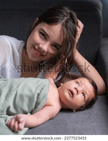 An older sister and her newborn little brother are lying on the sofa. The girl looks at the baby with love. Gently hugs the baby. Family, love, newborn